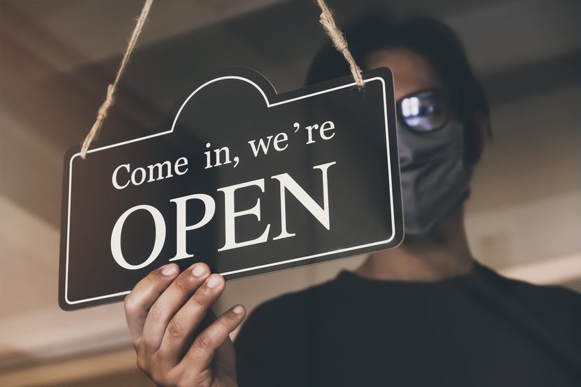 man with face mask turning an open sign on a business